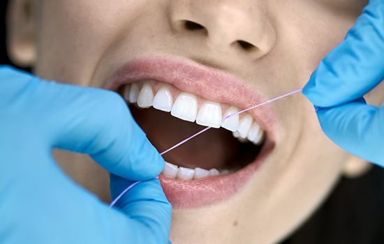 Dental hygienist with blue gloves flossing patient's teeth