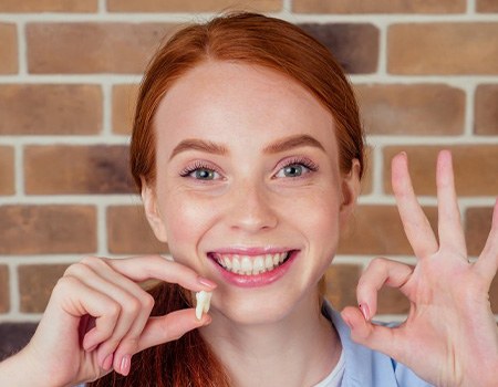 Woman holding a tooth and smiling on a brick background