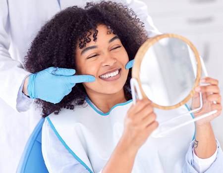 Dentist pointing at patient’s smile while she looks in the mirror